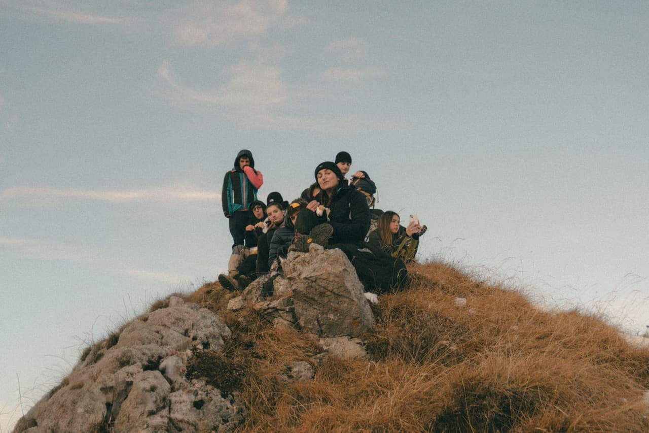 Group of friends sharing a snack break on a Dolomites summit at golden hour — community hiking experiences on weAltura